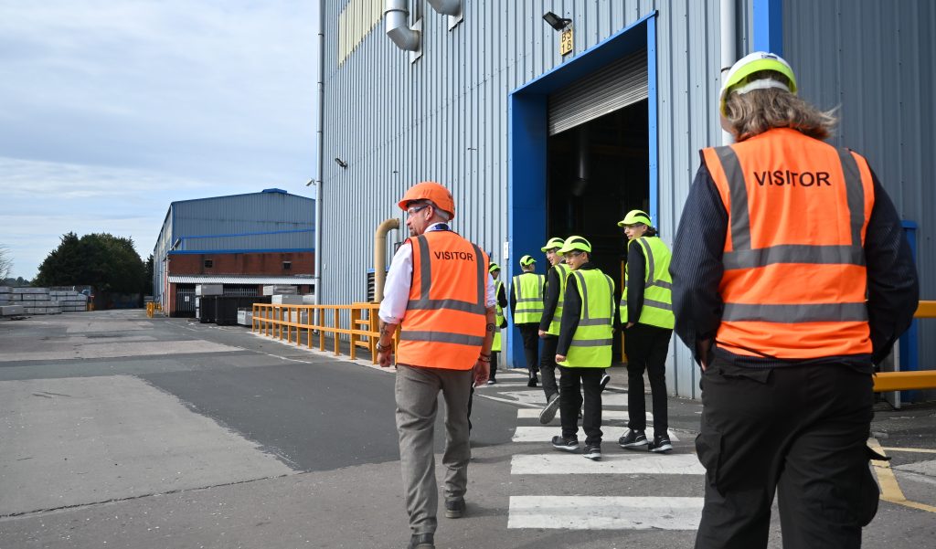 Students are shown around the exterior of a factory. All are wearing protective clothing.