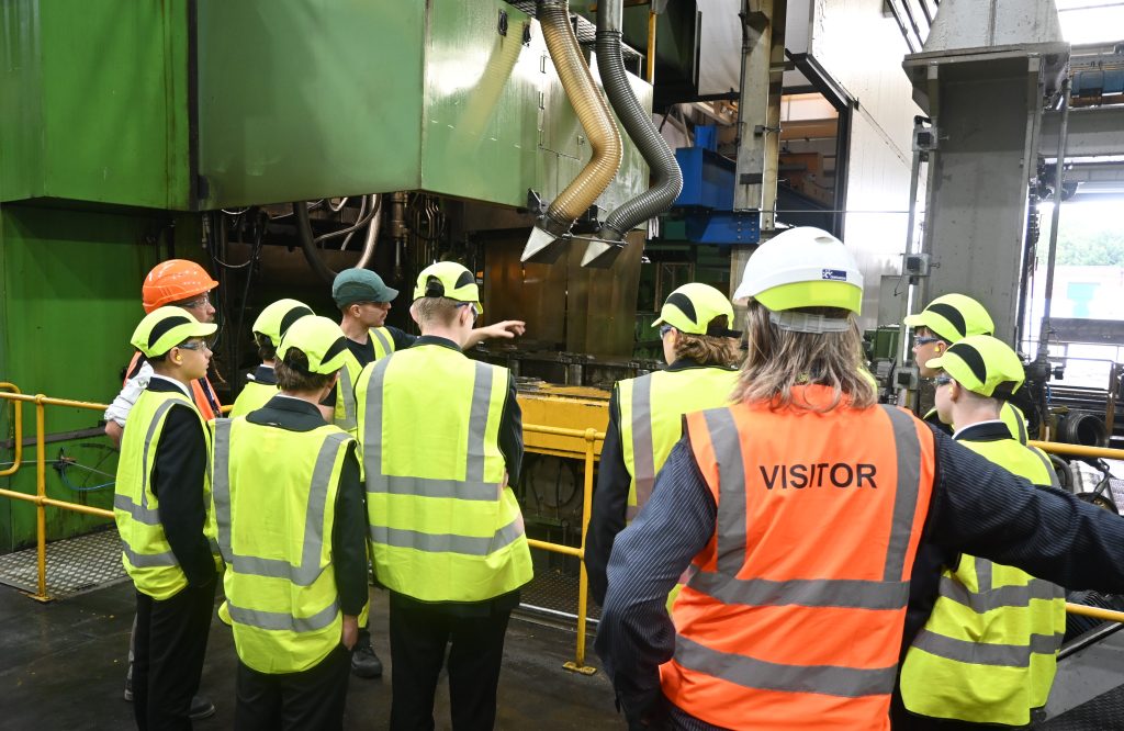A group of students being shown the machinery and equipment in a factory. All wearing protective clothing.