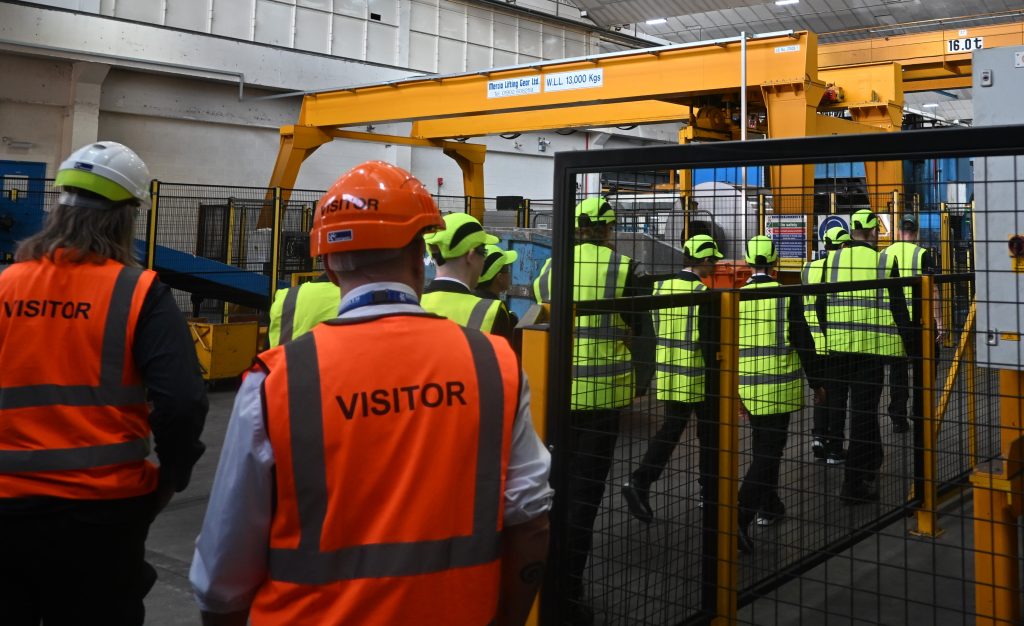 A group of students on a guided tour through a factory all wearing protective clothing.