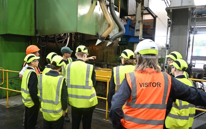 A group of students being shown the machinery and equipment in a factory. All wearing protective clothing.